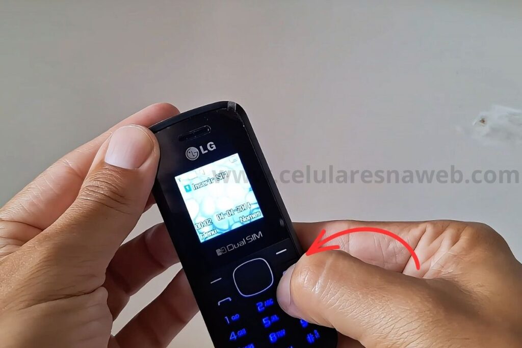 Frame de vídeo mostrando mãos segurando o celular LG B220 com a tela acesa exibindo a mensagem Inserir SIM. O polegar direito está posicionado sobre o teclado numérico do aparelho.